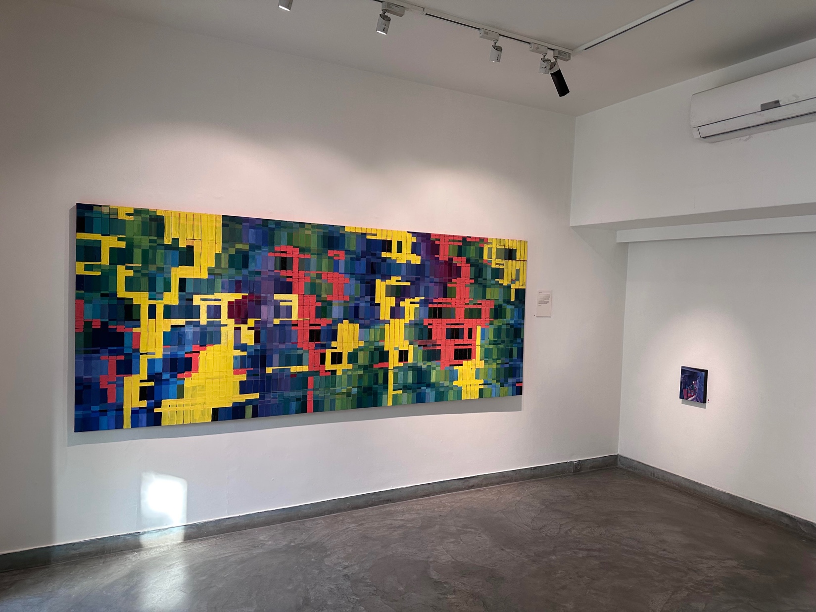 Installation view: the large grid painting on a white wall above the small dark canvas.